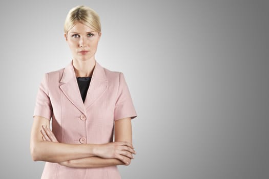 Portrait of a young businesswoman in formal pink with arms crossed against gray background