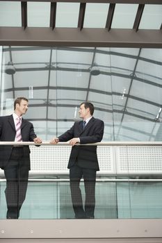 Two businessmen communicating while standing against railing in office