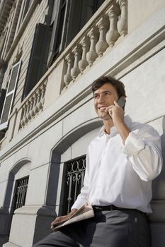 Mature businessman communicating on cell phone while leaning on the wall