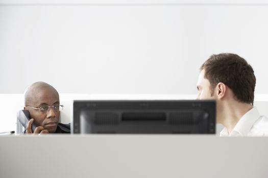 Two office workers sitting in office cubicle one using phone