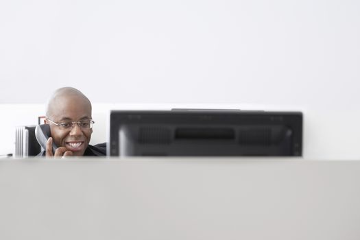 Smiling African American businessman using telephone at computer desk