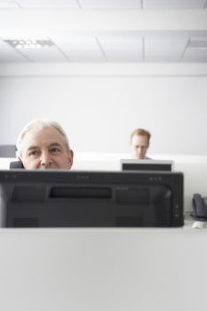 Middle aged businessman on call at computer desk with colleague in background