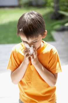 Young boy blowing nose in backyard