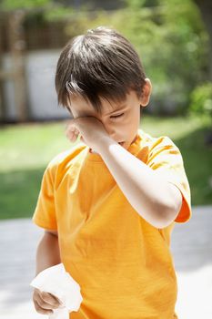 Young boy with tissue paper rubbing eye in backyard