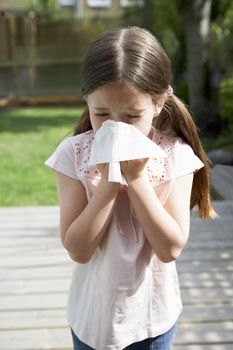 Young girl blowing nose with tissue paper in backyard