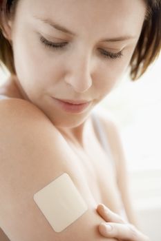 Closeup of young woman looking at nicotine patch on arm over white background