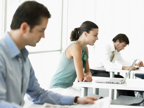 Side view of young businesswoman using laptop with male colleagues working in office