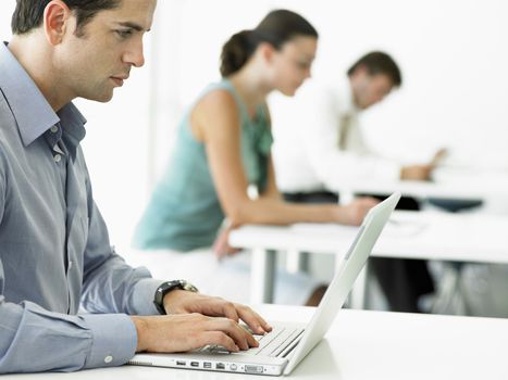Side view of young businessman using laptop with colleagues in background