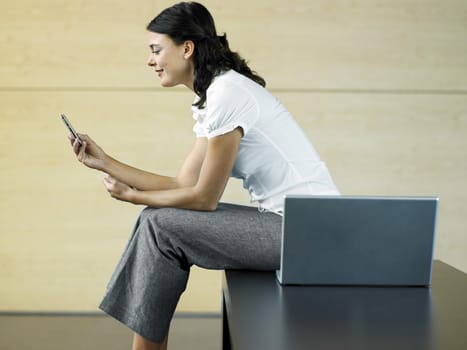 Side view of happy young businesswoman reading text message with laptop on bench in lobby