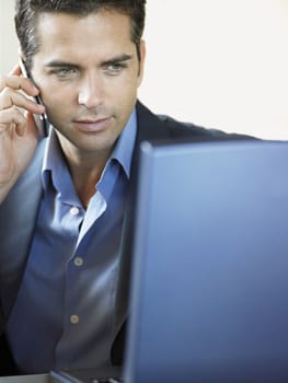 Young businessman on call while using laptop