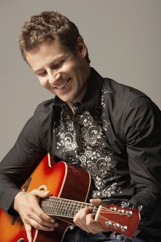 Happy young man playing guitar against gray background