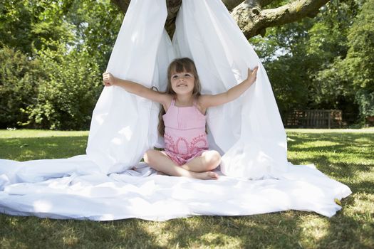 Young girl sitting in tent made of sheet in the backyard 