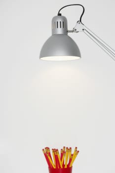 Pencil case below a lamp over white background