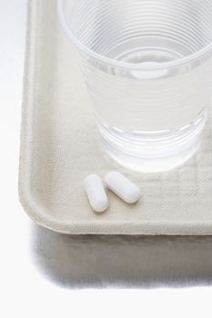 Two pills beside water in plastic cup on tray