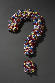 Various pills forming question mark on black background