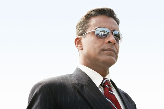Confident mature businessman in sunglasses looking at helicopter against clear sky