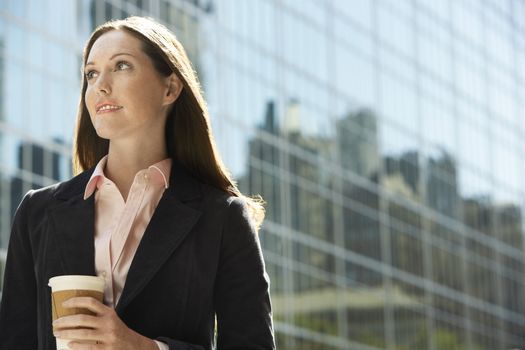 Contemplative female office worker with drink outside office building
