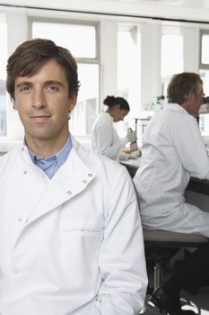 Portrait of young male scientist with colleagues working in background