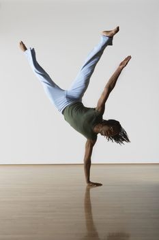 Young male dancer standing on one hand in rehearsal room