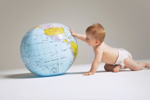 Side view of baby playing with globe isolated on colored background