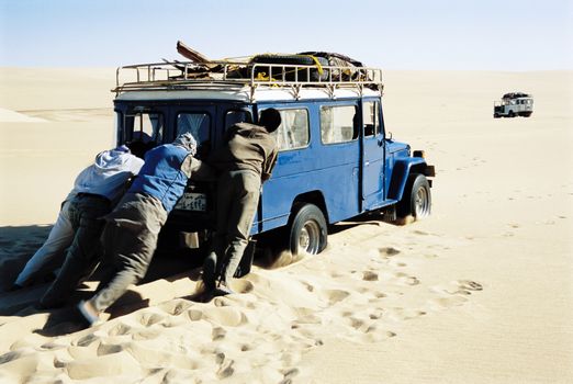 Men pushing jeep in desert