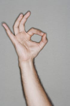 Closeup of a hand making okay sign against gray background