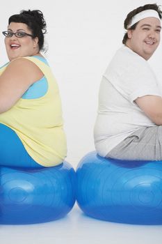 Side view of an overweight man and woman sitting on exercise balls