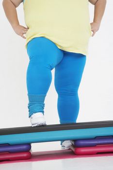 Low section of a plus size woman on exercise steps against white background