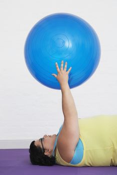 Side view of an overweight woman lying down and holding up exercise ball