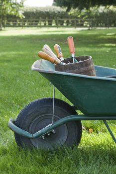 Closeup side view of cropped wheelbarrow with gardening tools on grass