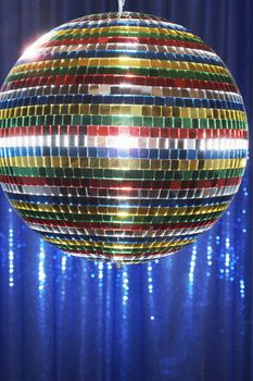Multi-coloured disco ball in front of blue stage curtain close up