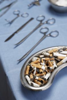 Cigarettes butts in medical tray with operating equipments on table