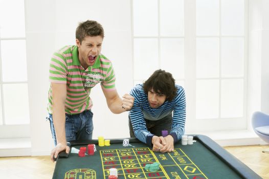 Young man celebrating gambling win at roulette table by friend
