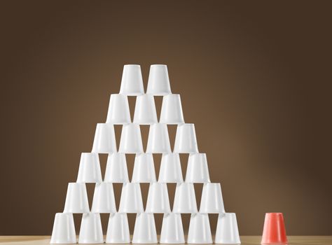 Pyramid of white plastic cups on table next to single red cup