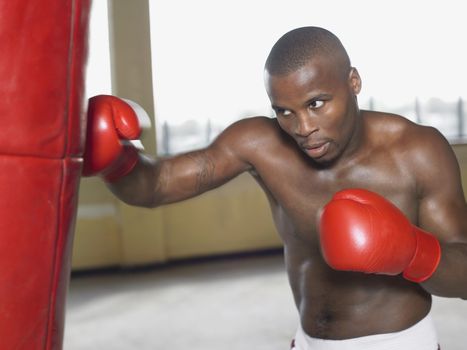 Shirtless African American boxer punching bag