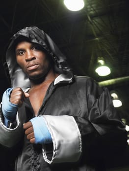 Portrait of an African American boxer in robe with hood up clenching fists