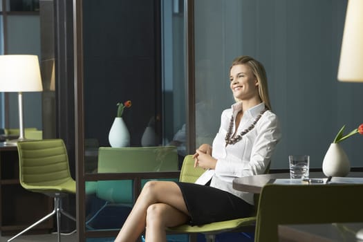 Happy young businesswoman sitting in office and smiling