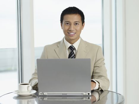 Portrait of a young businessman sitting at table with laptop and coffee