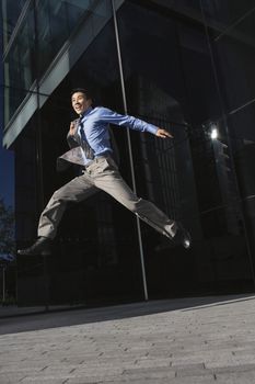 Low angle view of a young businessman with briefcase jumping outside office building
