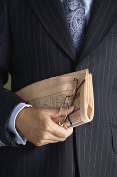 Closeup midsection of a businessman in suit holding glasses and newspaper