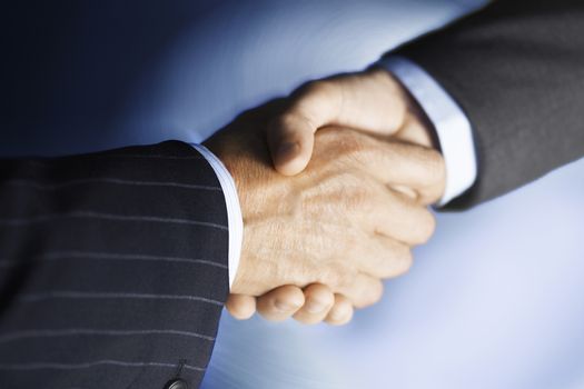 Closeup of businessmen shaking hands against blue background