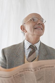 Senior man in spectacles reading newspaper half length