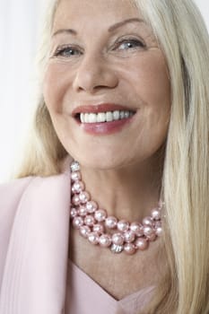 Closeup of a happy and glamorous senior woman smiling against white background