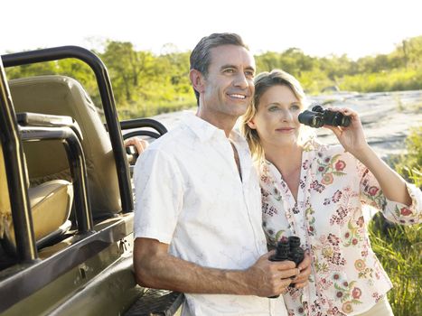 Smiling adult couple standing by jeep with binoculars 
