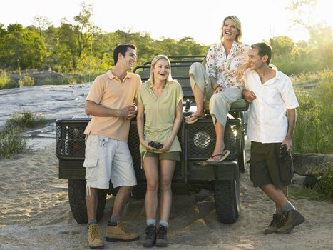 Full length group portrait of four cheerful people by jeep
