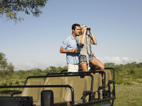Young couple on safari standing in jeep and looking through binoculars