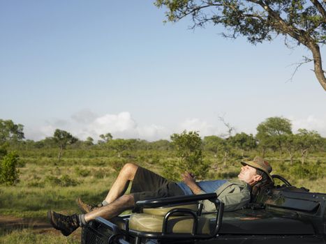 Side view of an adult man lying on bonnet of jeep in meadow