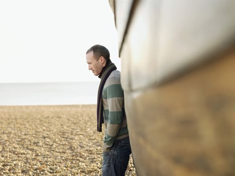 Side view of a man leaning against wooden hull of boat on beach