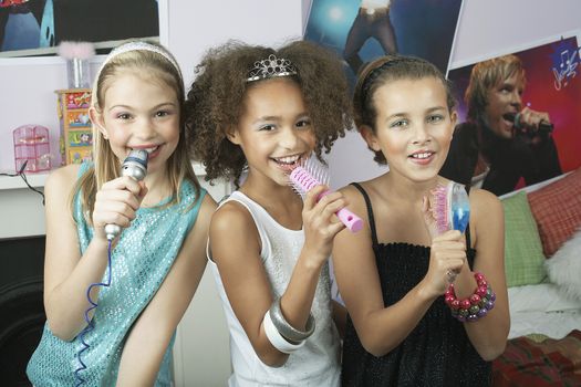 Multiethnic young girls using brushes as microphones to sing at a slumber party