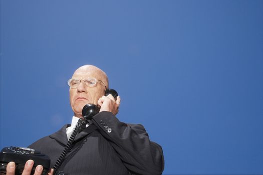 Low angle view of senior businessman using telephone against clear sky